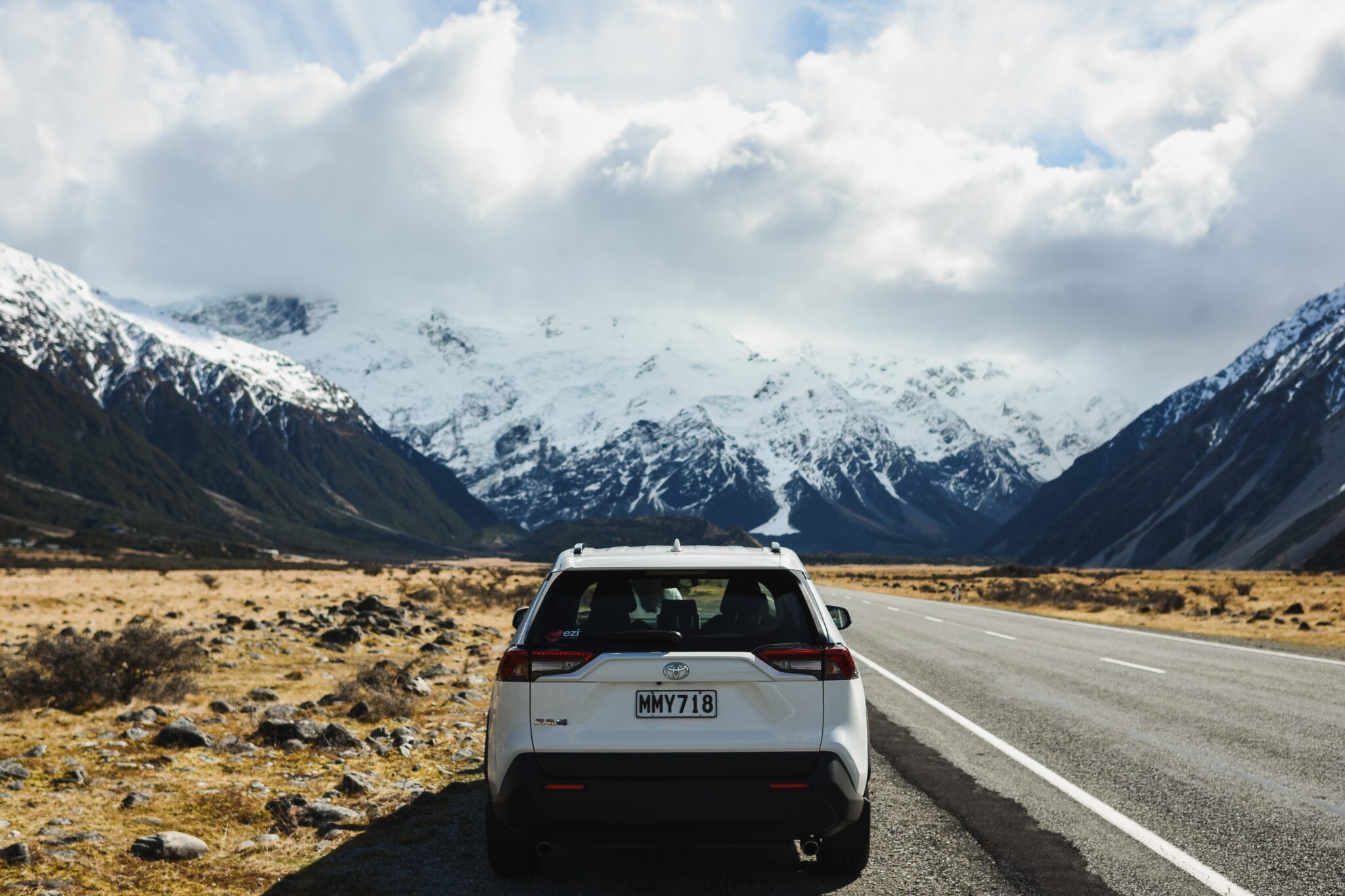 Car on the side of the road facing white capped mountains